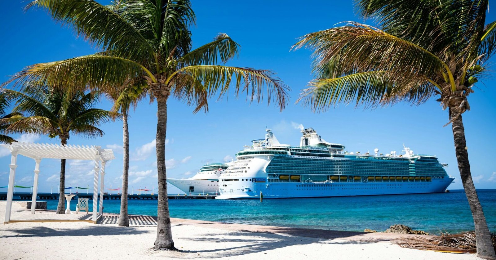 Eine Aufnahme von Palmen und zwei Royal Caribbean-Schiffen am Pier von Coco Cay, der Privatinsel von RCI.