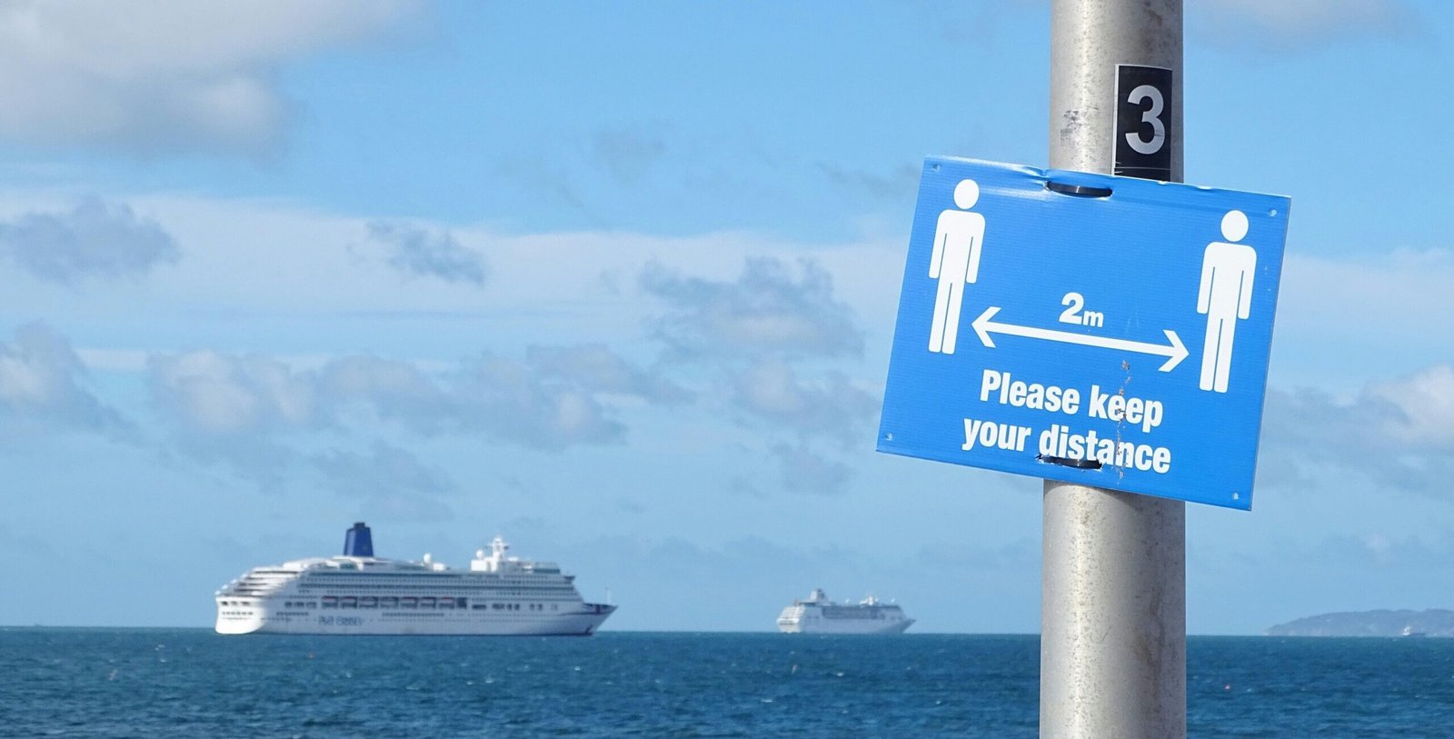 Eine Aufnahme von einem Hinweisschild zu Corona mit Kreuzfahrtschiffen im Hintergrund.